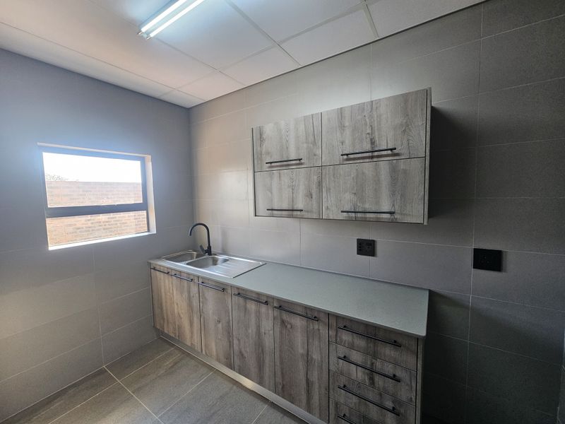 A modern, clean scullery area featuring wood-look cabinetry, a stainless steel sink, and neutral tiled finishes, providing a functional and well-maintained utility space.