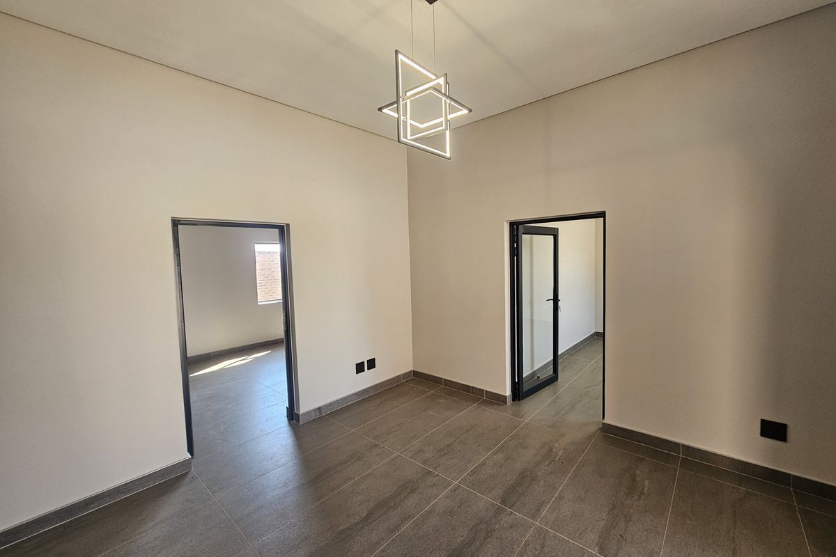 A bright, modern, and empty living space featuring neutral walls, large format floor tiles, and a contemporary geometric light fixture.