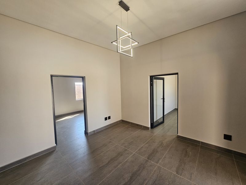 A bright, modern, and empty living space featuring neutral walls, large format floor tiles, and a contemporary geometric light fixture.
