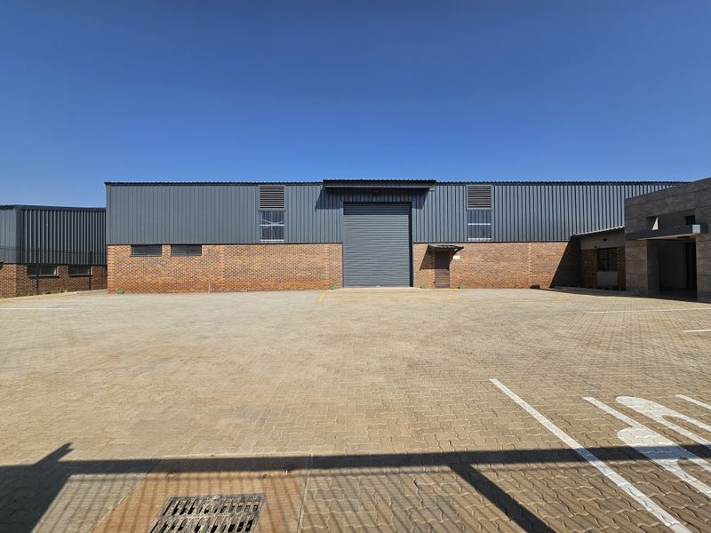 Industrial warehouse exterior featuring a large roller shutter door, brick and metal cladding facade, and a spacious paved parking area.