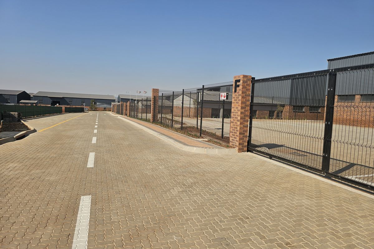 View of an industrial park entrance featuring paved access roads, secure perimeter fencing with brick pillars, and modern warehouse structures.