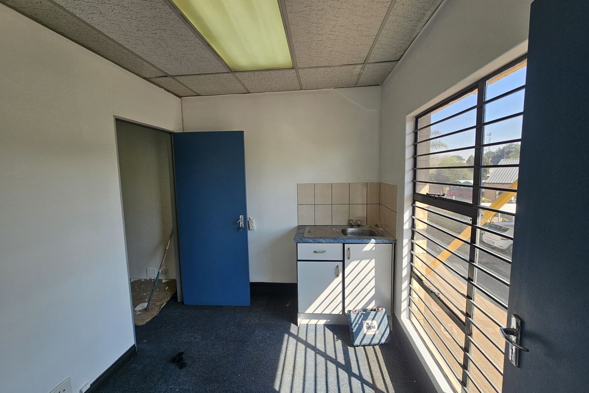 A small, functional kitchenette area featuring a sink, base cabinetry, tiled backsplash, and security bars on the window, suitable for office or utility use.