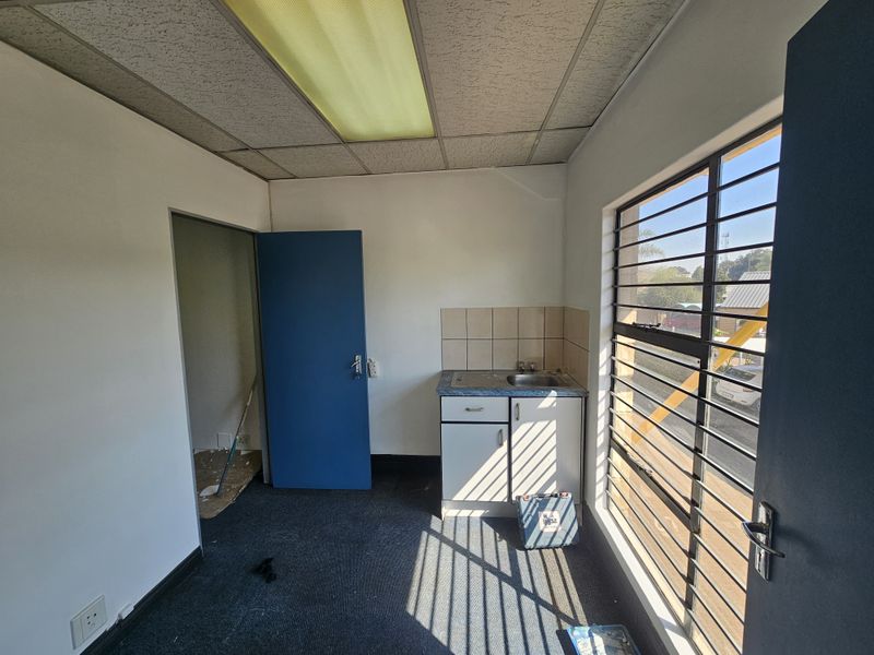 A small, functional kitchenette area featuring a sink, base cabinetry, tiled backsplash, and security bars on the window, suitable for office or utility use.