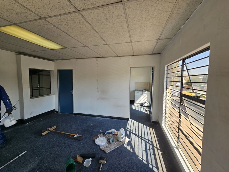 An industrial office space featuring a suspended ceiling, security bars on windows, and carpet flooring, currently undergoing maintenance and painting.