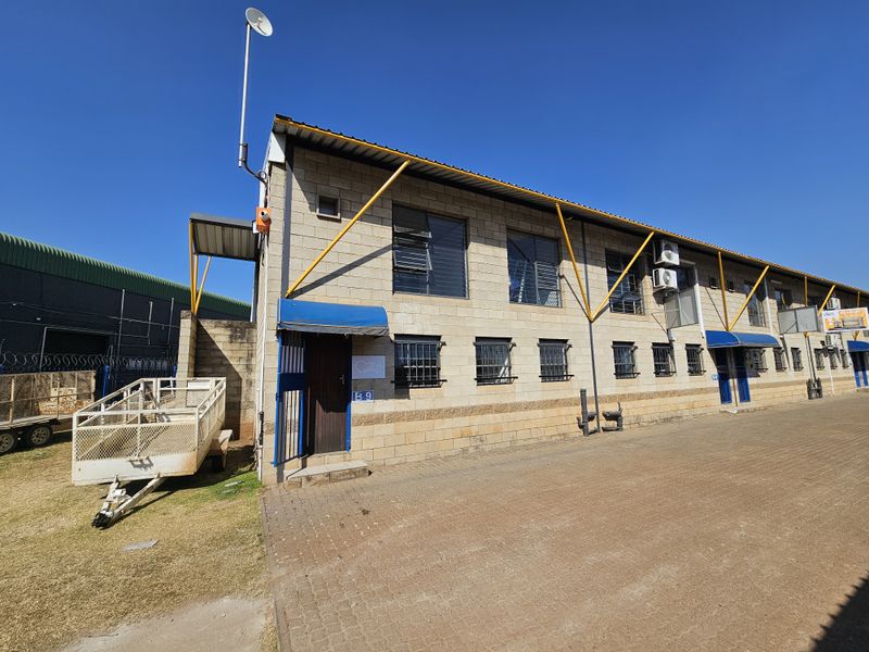 Exterior view of an industrial unit featuring concrete block construction, steel support beams, security window bars, and paved access area.
