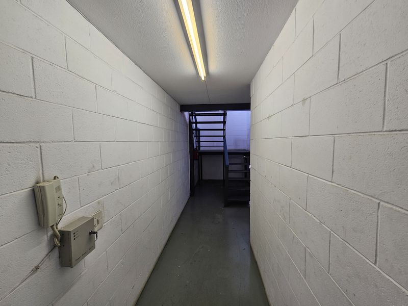A functional industrial hallway featuring painted concrete block walls, a metal staircase, and integrated fluorescent lighting.