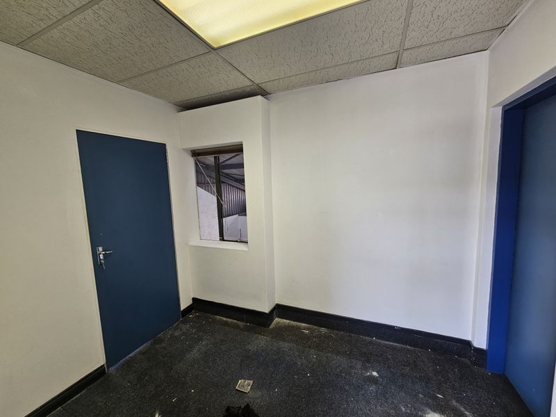 An empty office space featuring a suspended ceiling, recessed lighting, and an internal window, requiring minor cosmetic updates to the flooring and walls.