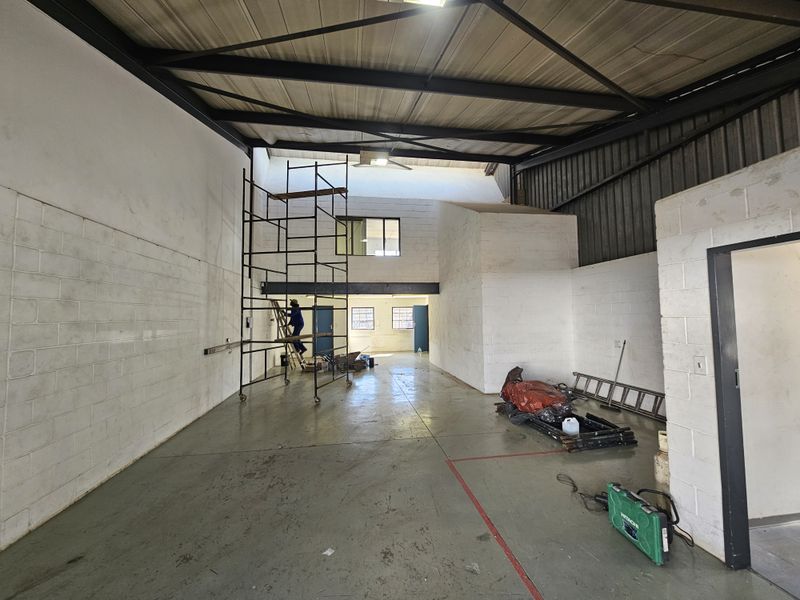 Spacious industrial utility area featuring high ceilings with exposed steel trusses, painted concrete block walls, and durable epoxy-coated flooring with a mezzanine level.