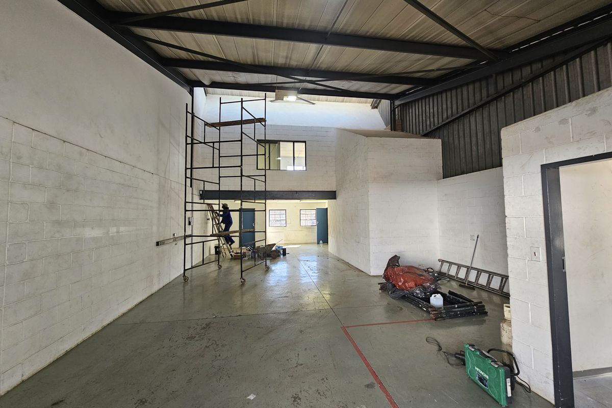 Spacious industrial utility area featuring high ceilings with exposed steel trusses, painted concrete block walls, and durable epoxy-coated flooring with a mezzanine level.