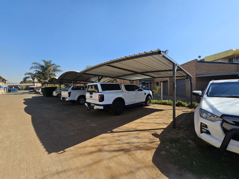 Industrial property exterior featuring a covered parking area with metal carports and paved driveway access.