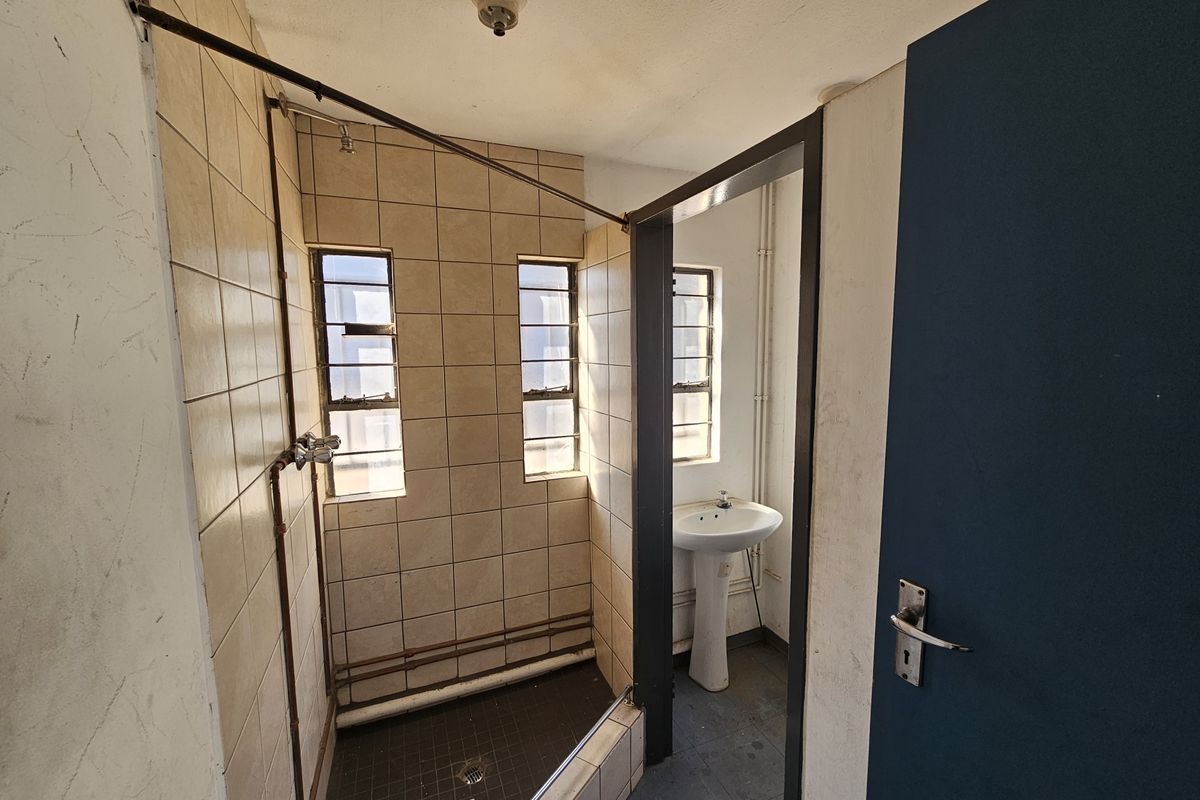 A functional bathroom featuring a tiled shower enclosure, pedestal sink, and steel frame windows, requiring cosmetic updates to improve its overall condition.