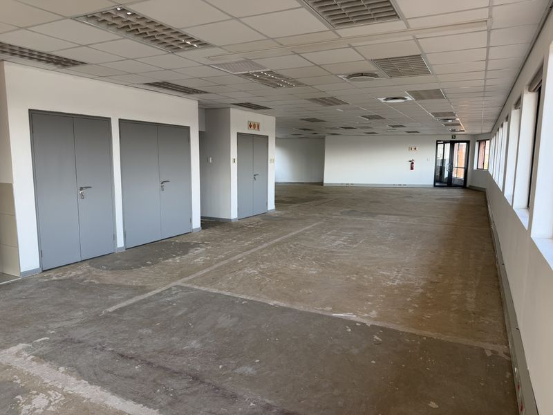A large, open-plan office space featuring a suspended ceiling, recessed lighting, and expansive windows, currently awaiting flooring installation and final fit-out.