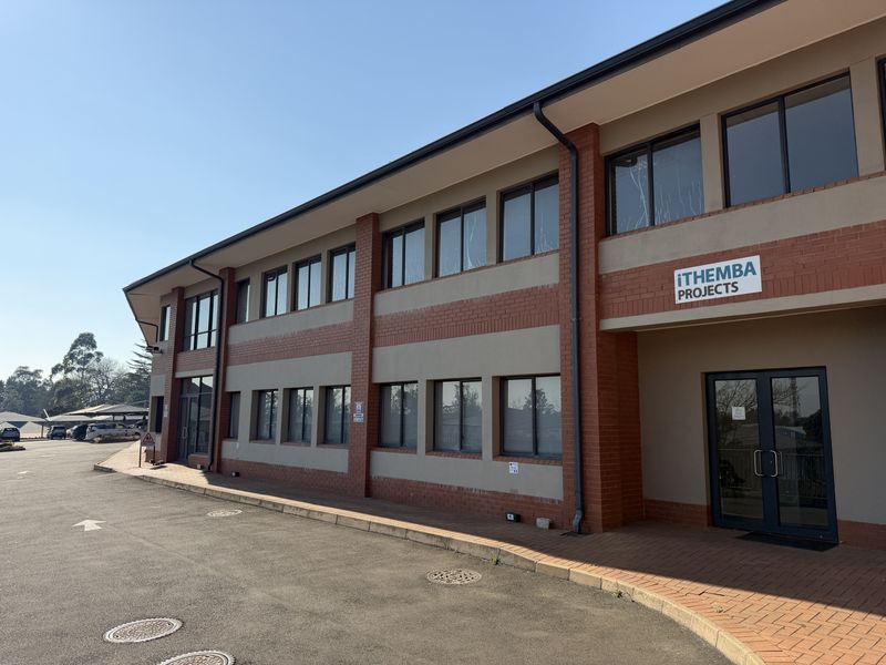 A well-maintained two-story office building featuring a brick and plaster facade, aluminium windows, and a paved entrance area with adjacent asphalt parking.