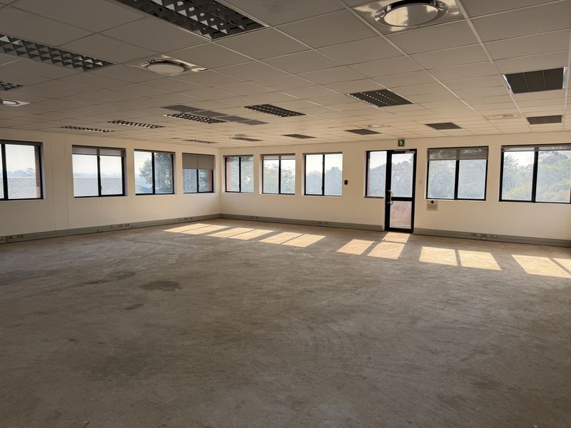 A spacious, open-plan office area featuring a suspended ceiling, recessed lighting, and extensive window frontage, currently awaiting final flooring installation.
