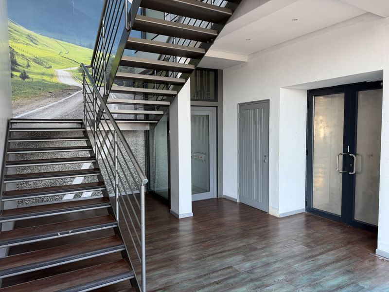 Modern office entrance area featuring a sleek metal staircase, laminate flooring, and glass-paneled doors providing a clean and professional welcome.