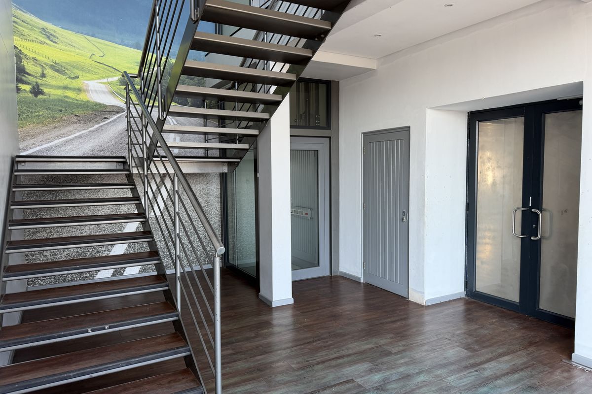 Modern office entrance area featuring a sleek metal staircase, laminate flooring, and glass-paneled doors providing a clean and professional welcome.