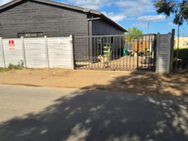 Front exterior view of an industrial property featuring a dark-painted building, secure metal gate, and precast concrete perimeter wall.