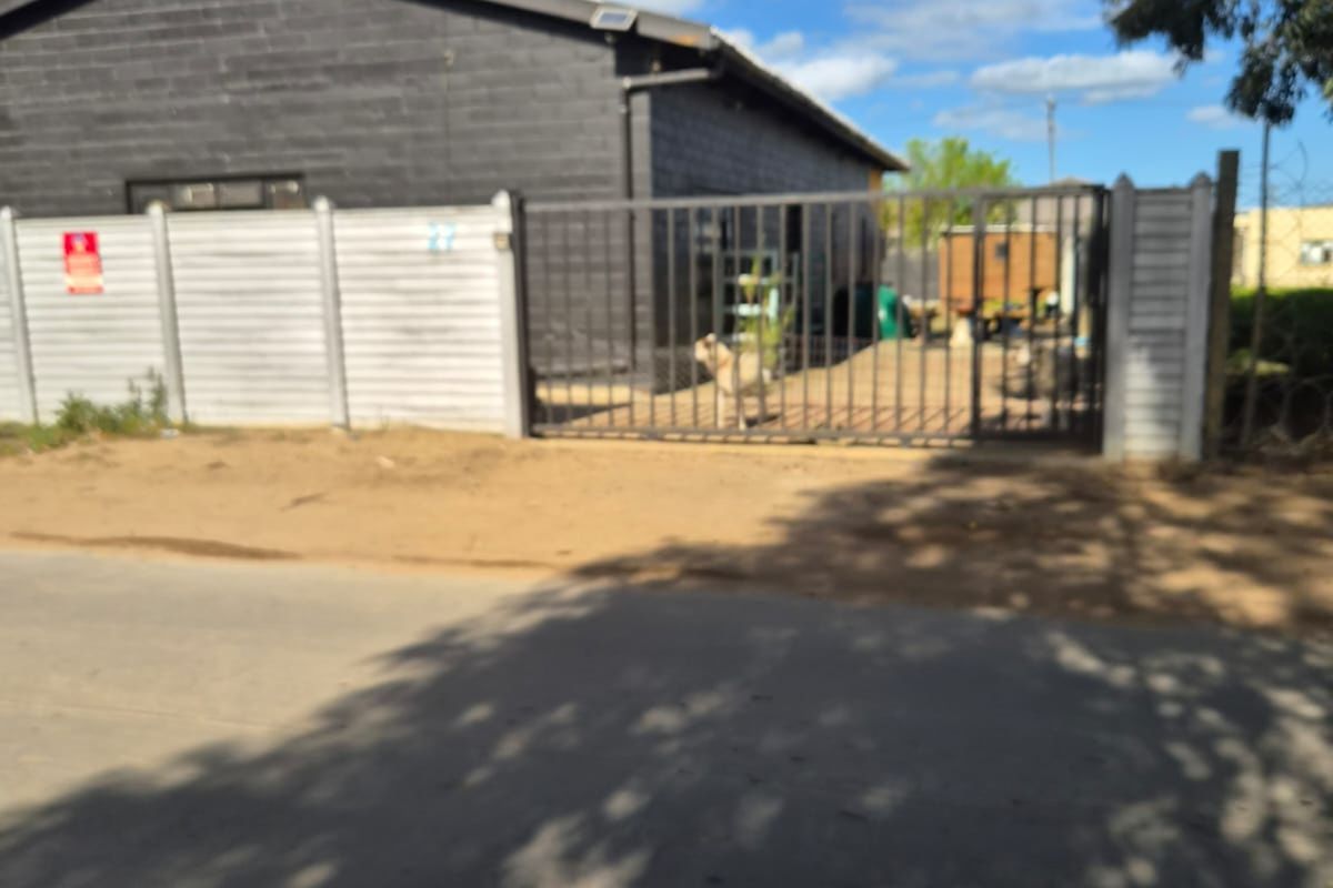 Front exterior view of an industrial property featuring a dark-painted building, secure metal gate, and precast concrete perimeter wall.