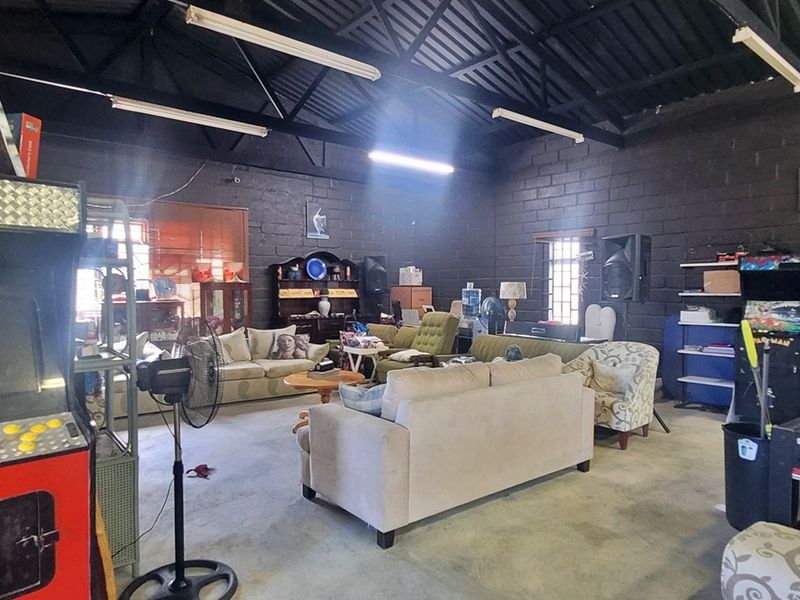 Spacious industrial-style utility area featuring exposed steel roof trusses, painted concrete block walls, and durable concrete flooring, suitable for various commercial or recreational uses.