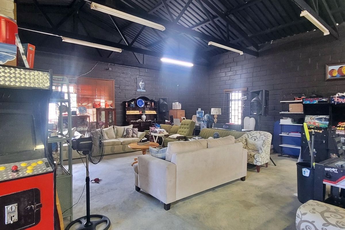 Spacious industrial-style utility area featuring exposed steel roof trusses, painted concrete block walls, and durable concrete flooring, suitable for various commercial or recreational uses.
