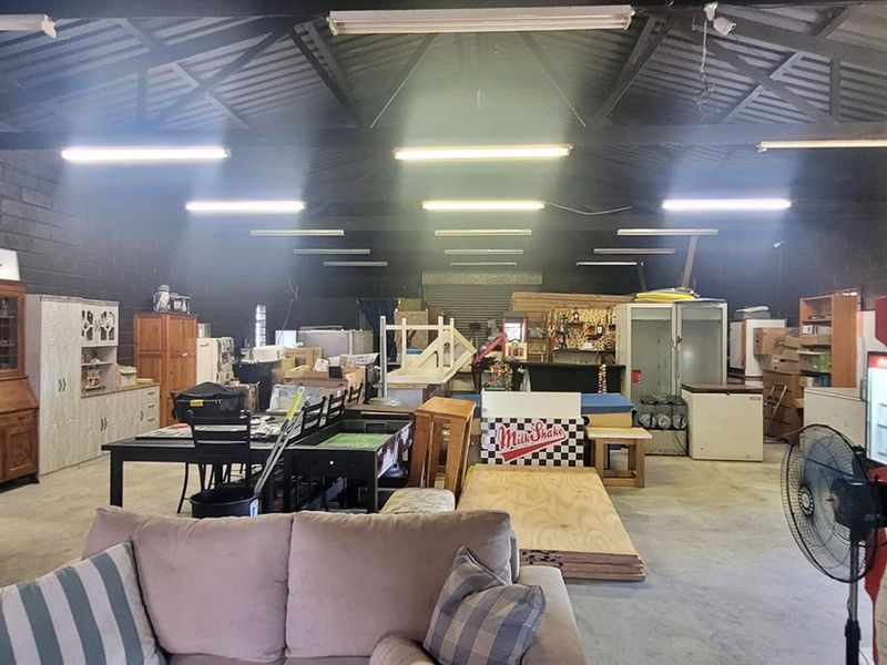 Spacious industrial utility area featuring exposed steel roof trusses, concrete flooring, and high-output fluorescent lighting, suitable for workshop or storage use.