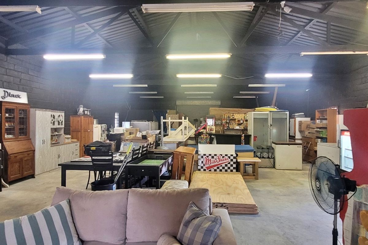 Spacious industrial utility area featuring exposed steel roof trusses, concrete flooring, and high-output fluorescent lighting, suitable for workshop or storage use.