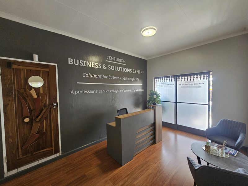 A professional office reception area featuring a modern desk, laminate flooring, and a decorative wooden door with a frosted glass entrance partition.