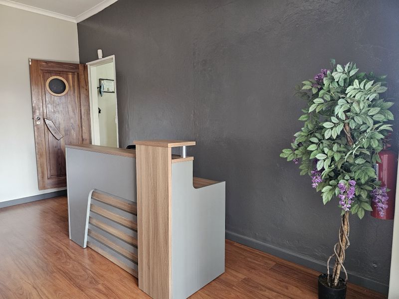 A professional office reception area featuring laminate flooring, a modern reception desk, and a solid timber door with a circular window detail.