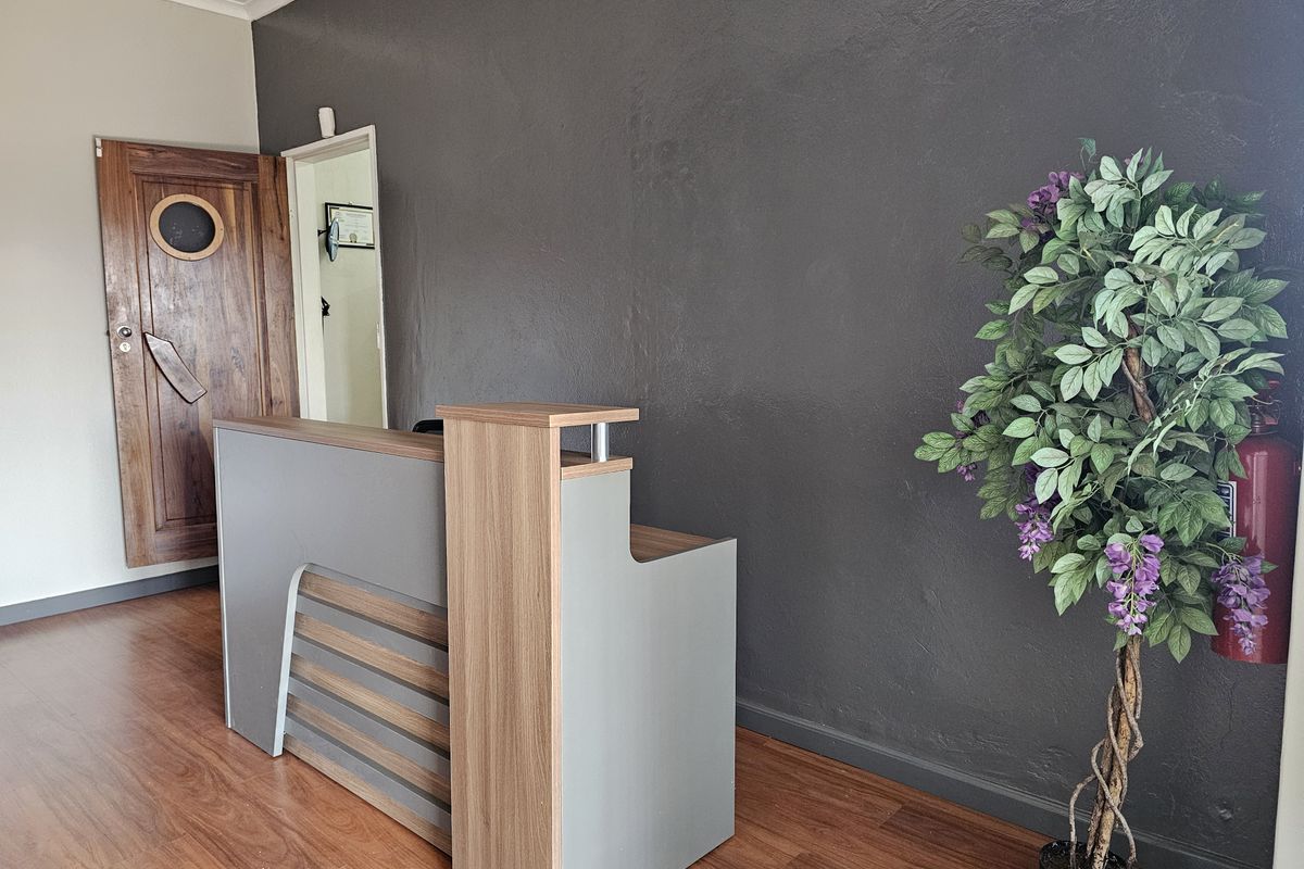 A professional office reception area featuring laminate flooring, a modern reception desk, and a solid timber door with a circular window detail.