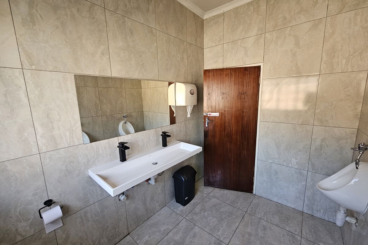A clean, modern office bathroom featuring full-height wall tiling, a wall-mounted basin with black fixtures, and a wall-mounted urinal.