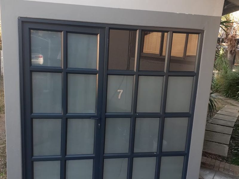 A modern office entrance featuring a dark-framed frosted glass door and a stone-tiled patio area.