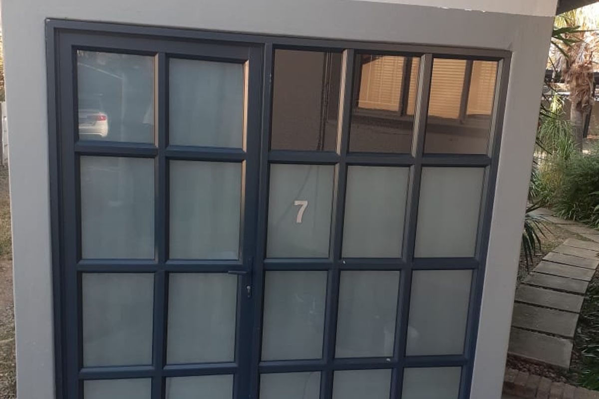 A modern office entrance featuring a dark-framed frosted glass door and a stone-tiled patio area.