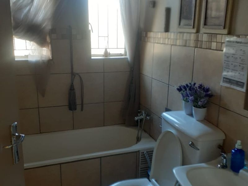 A functional bathroom featuring a bathtub, toilet, and washbasin with tiled finishes and security bars on the windows.