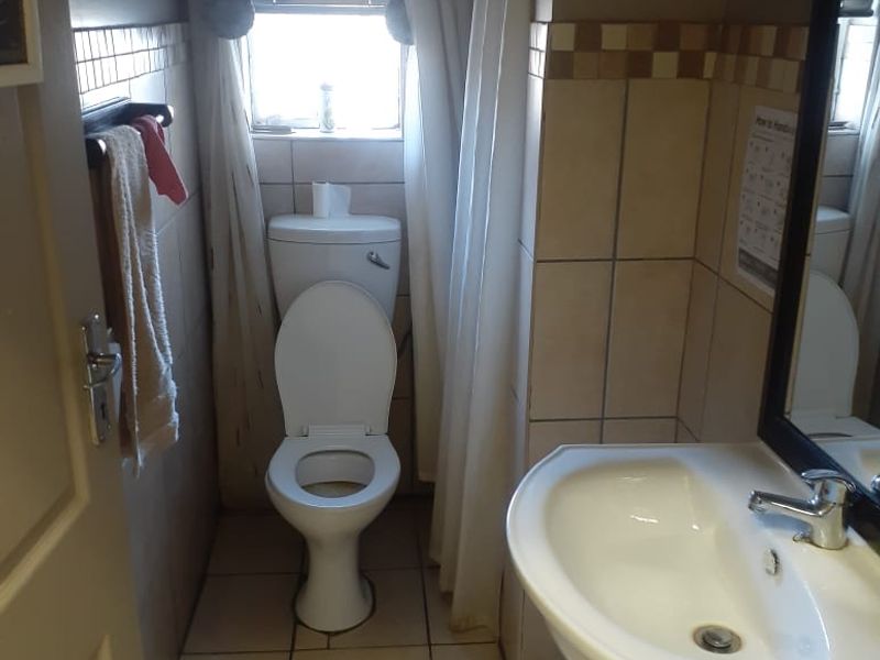 A compact bathroom featuring a toilet, pedestal basin, and tiled finishes. The space is functional but would benefit from cosmetic updates.