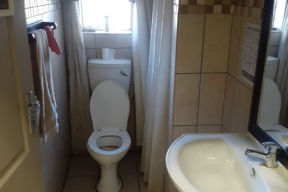 A compact bathroom featuring a toilet, pedestal basin, and tiled finishes. The space is functional but would benefit from cosmetic updates.