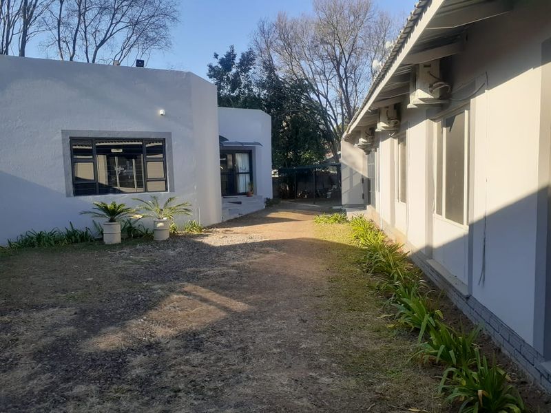 Rear exterior view of the office property featuring a paved walkway between buildings, established garden beds, and wall-mounted air conditioning units.