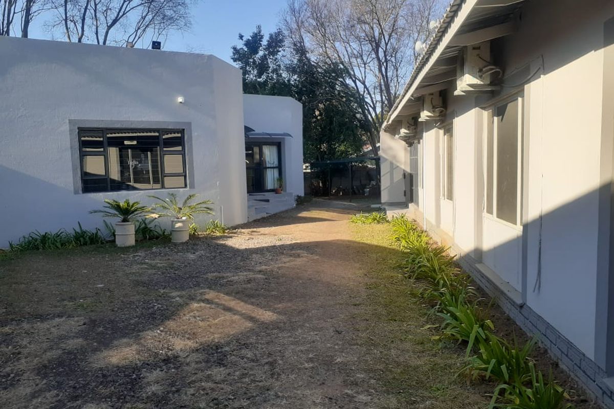 Rear exterior view of the office property featuring a paved walkway between buildings, established garden beds, and wall-mounted air conditioning units.