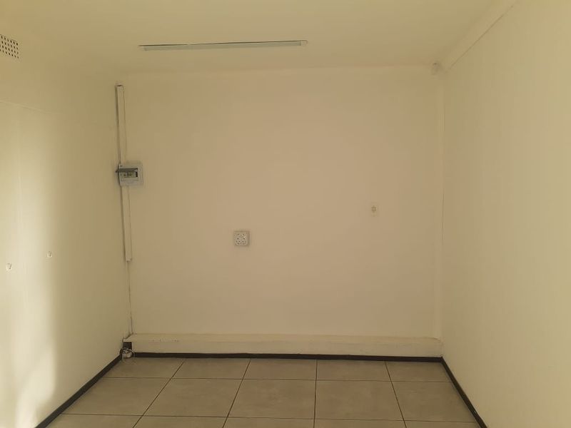 A vacant office space featuring tiled flooring, surface-mounted electrical infrastructure, and a basic lighting fixture.