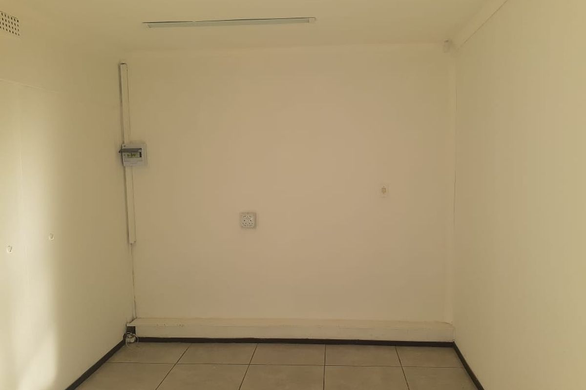 A vacant office space featuring tiled flooring, surface-mounted electrical infrastructure, and a basic lighting fixture.