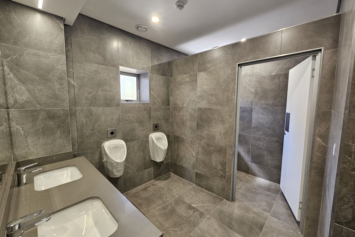 Modern industrial-style commercial bathroom featuring dual vanity sinks, wall-mounted urinals, and high-quality grey porcelain tiling throughout.
