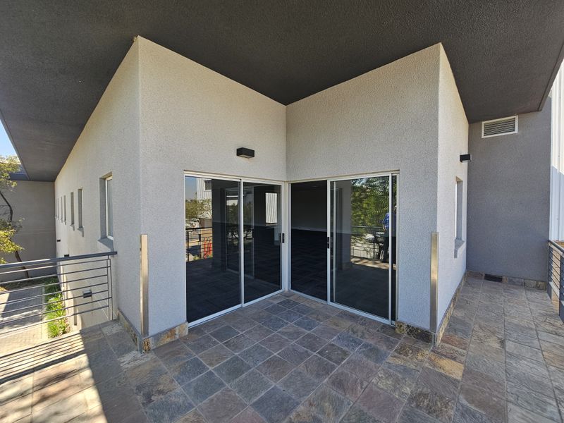 A modern industrial balcony featuring stone tile flooring, metal railings, and large sliding glass doors providing access to the interior space.