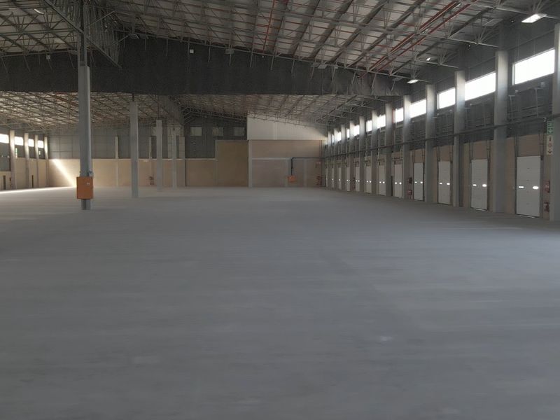 A large, open-plan industrial warehouse space featuring high ceilings, concrete flooring, and multiple roller shutter doors for efficient logistics and storage operations.