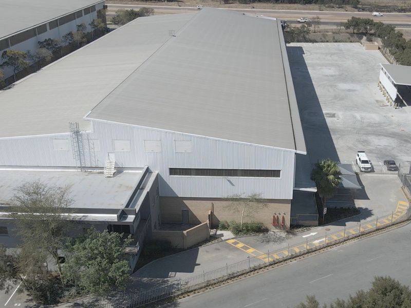 Aerial view of an industrial property featuring a large warehouse with metal roofing, concrete yard space, and secure perimeter fencing.