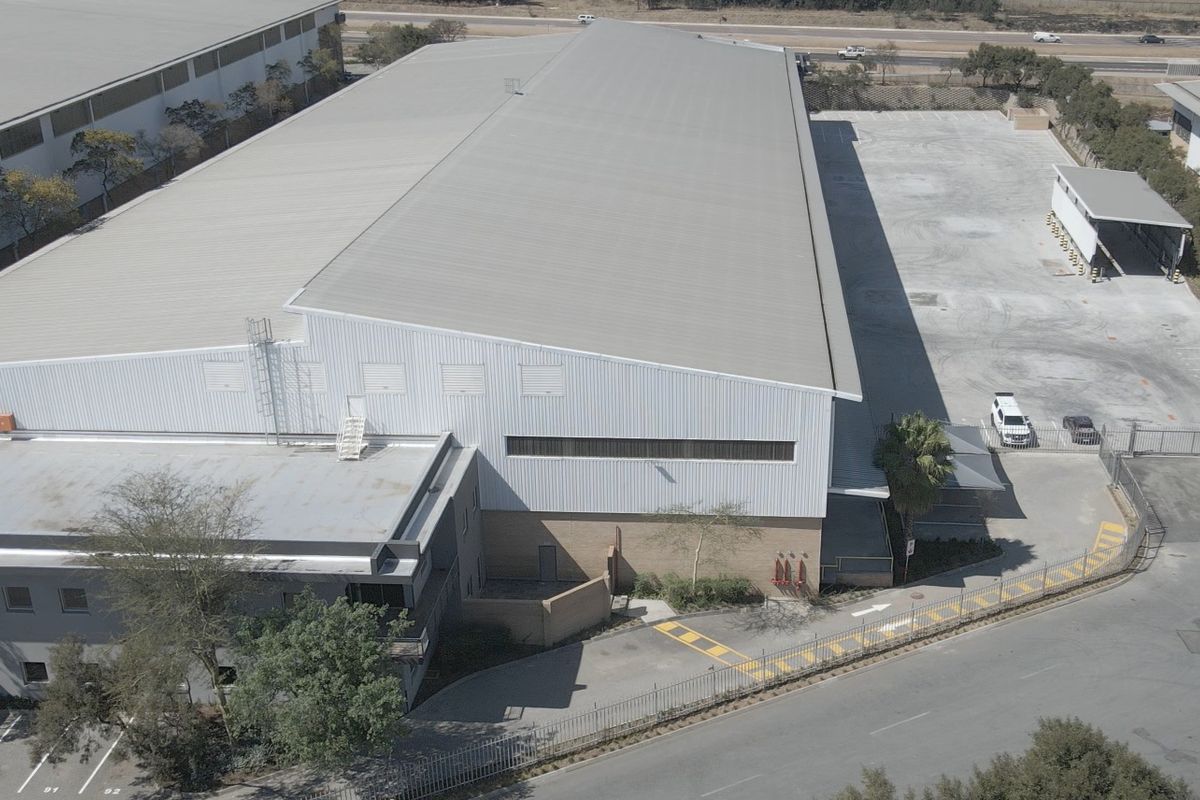 Aerial view of an industrial property featuring a large warehouse with metal roofing, concrete yard space, and secure perimeter fencing.