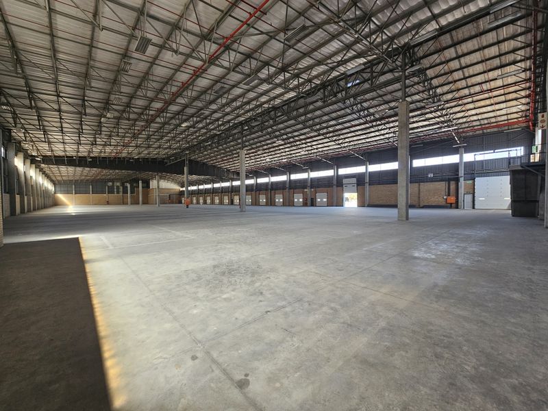Spacious industrial warehouse featuring high ceilings, concrete flooring, steel truss roofing, fire sprinkler system, and multiple roller shutter doors for efficient logistics access.