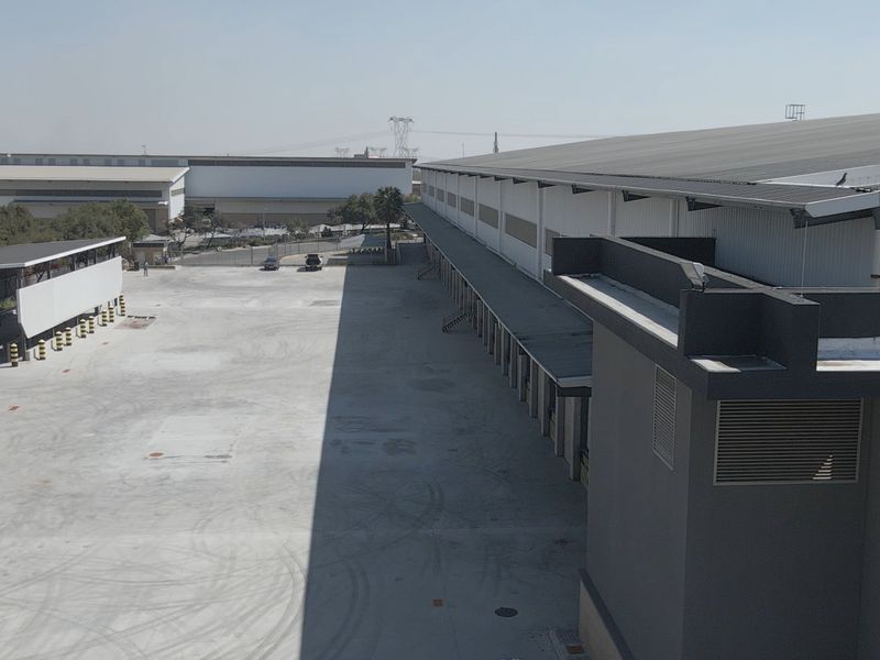Aerial view of an industrial facility featuring a large concrete yard, multiple loading bays, and extensive metal roofing structures.