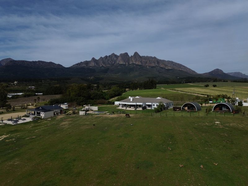 Aerial view of a sprawling farm property featuring a main residence, outbuildings, swimming pool, and expansive pastures set against a dramatic mountain backdrop.