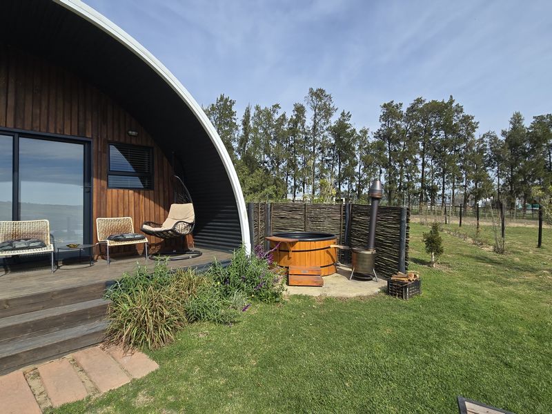 A modern timber-clad cabin featuring a spacious wooden deck, sliding glass doors, and a private wood-fired hot tub set in a landscaped garden.