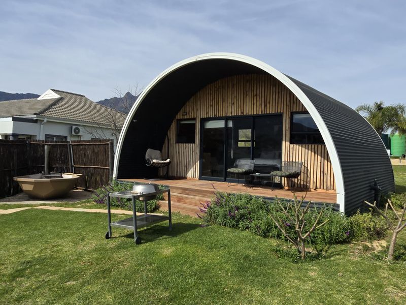 A modern, curved-roof cabin featuring timber cladding, a private wooden deck, and an outdoor wood-fired hot tub set within a landscaped garden.