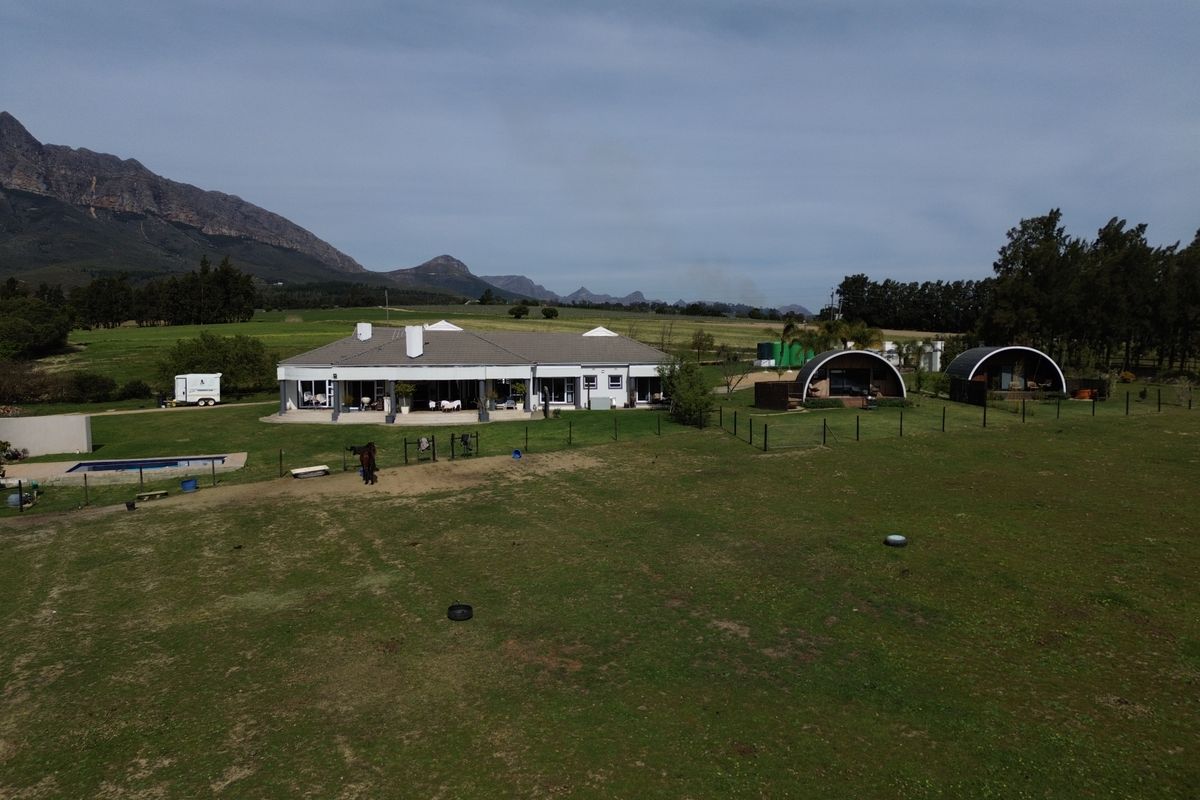 Aerial view of a farm property featuring a main residence with a patio, a swimming pool, and additional outbuildings set against a mountain landscape.